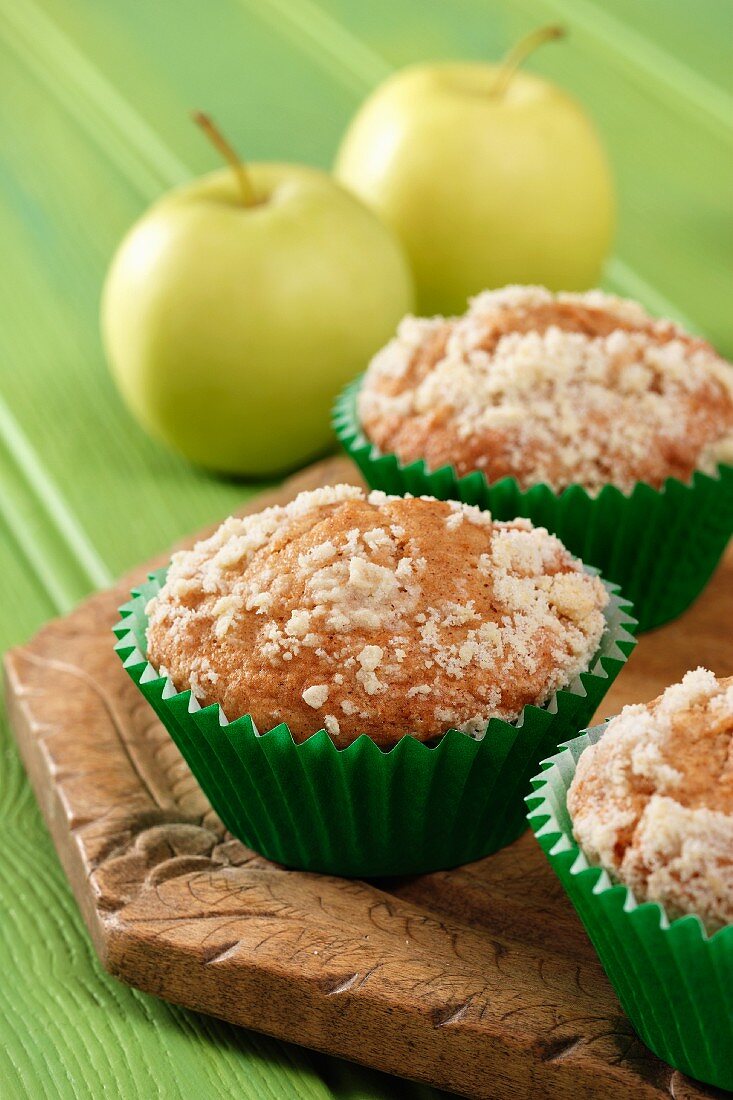 Apple streusel muffins on a wooden board with yellow apples all sitting on a green background.