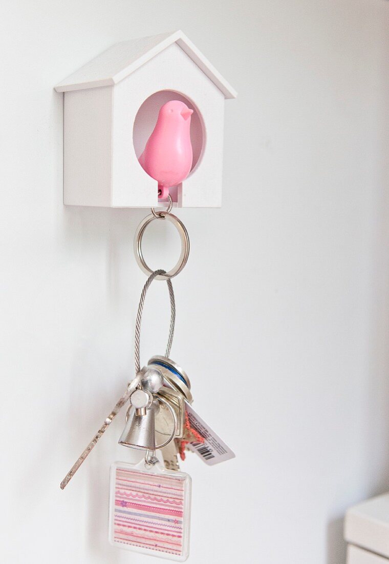Pink bird key chain pendant hung up in small white birdhouse