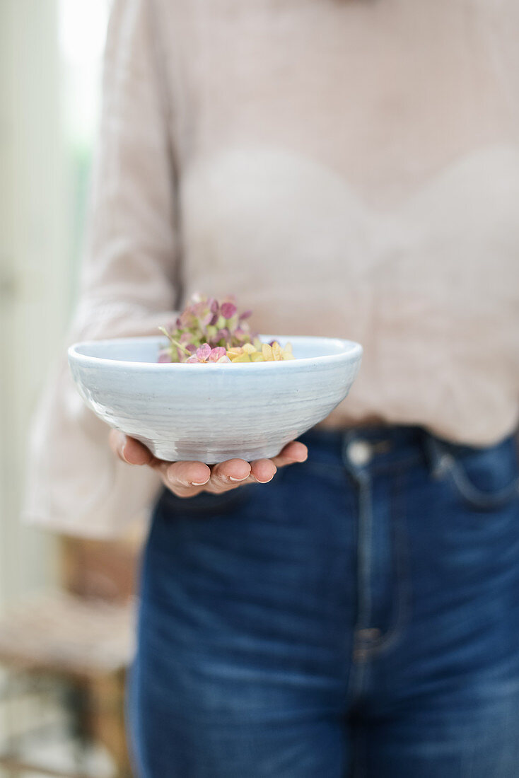 Frau hält Schale mit Hortensienblüten