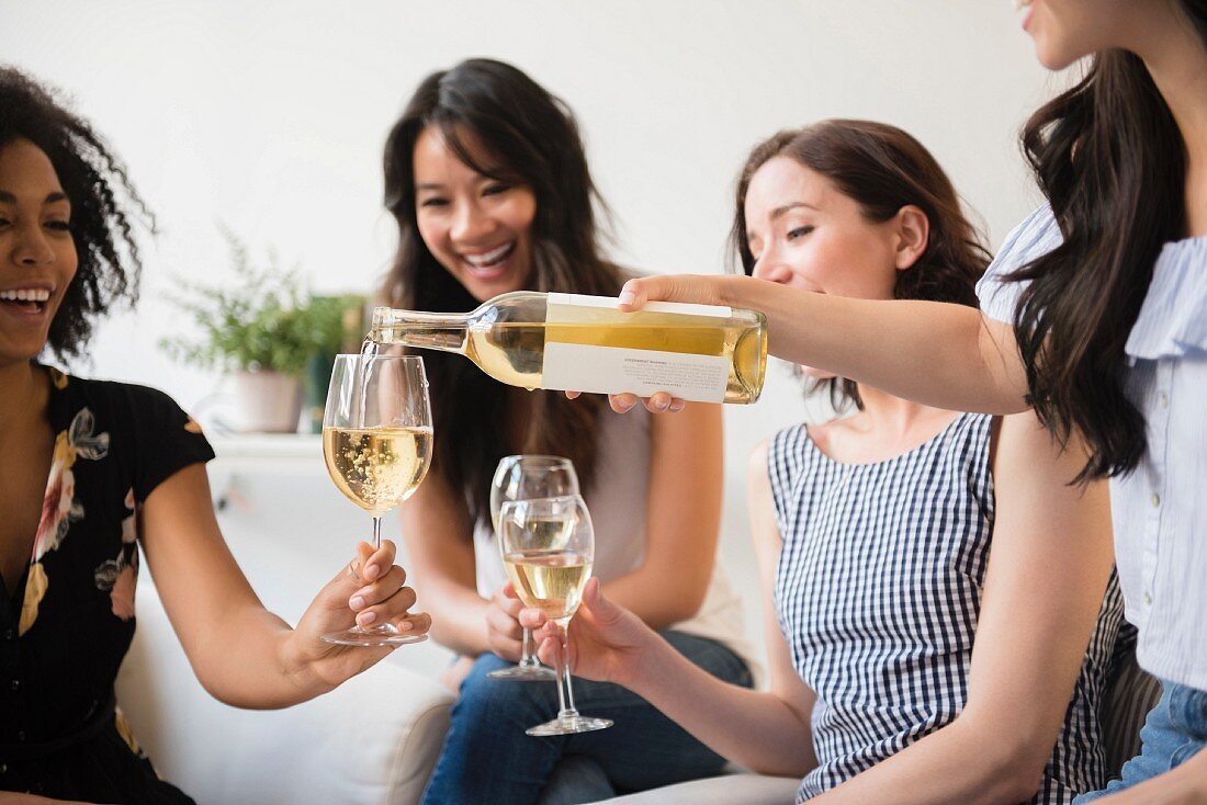Frau schenkt Freunden Weißwein ein