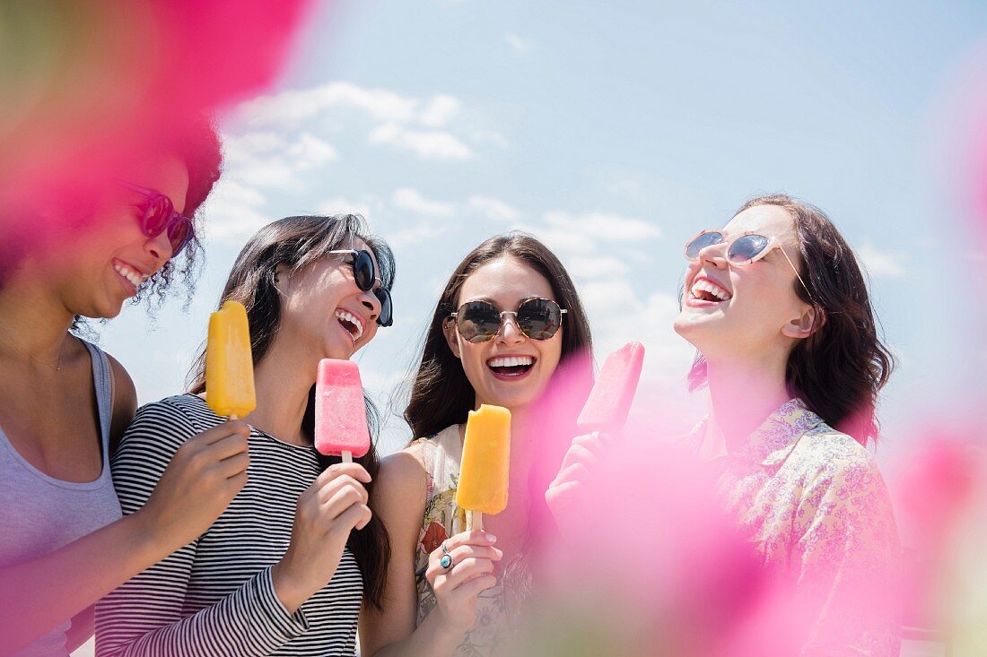 Laughing women eating flavored ice outdoors