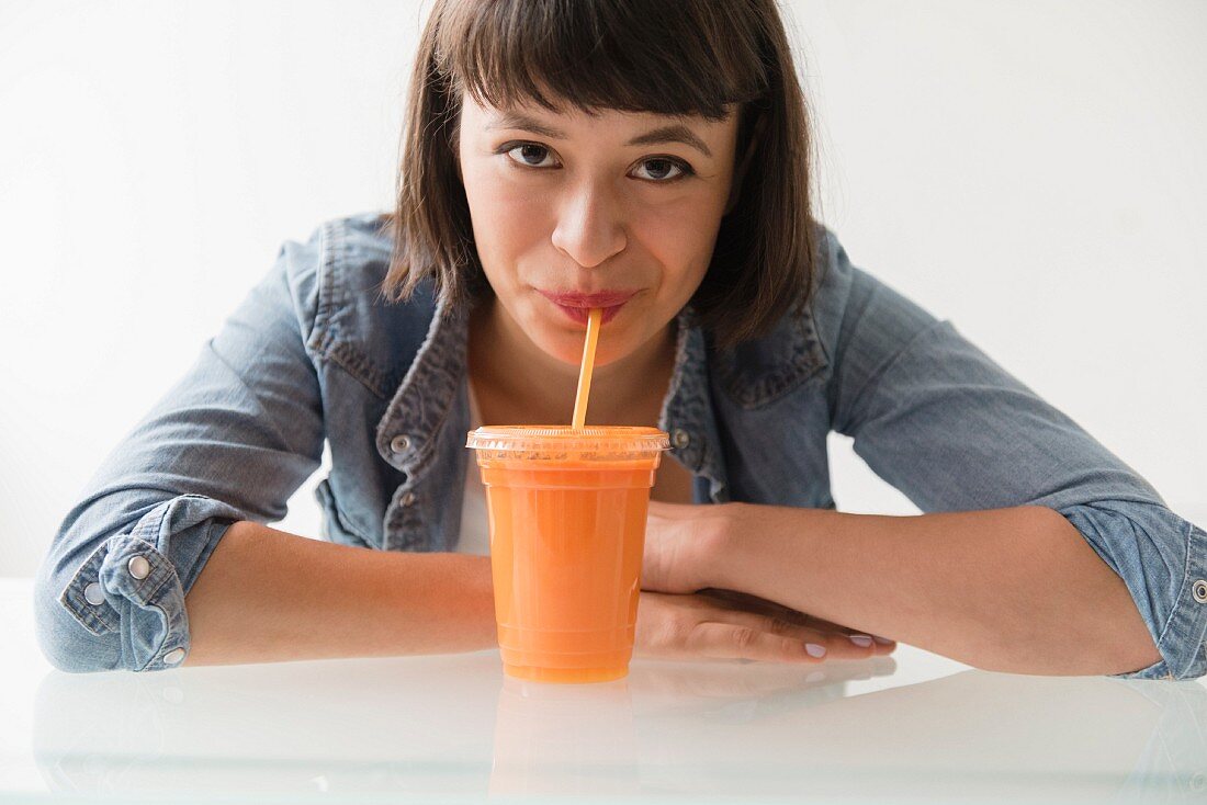 Hispanic woman drinking orange smoothie with straw