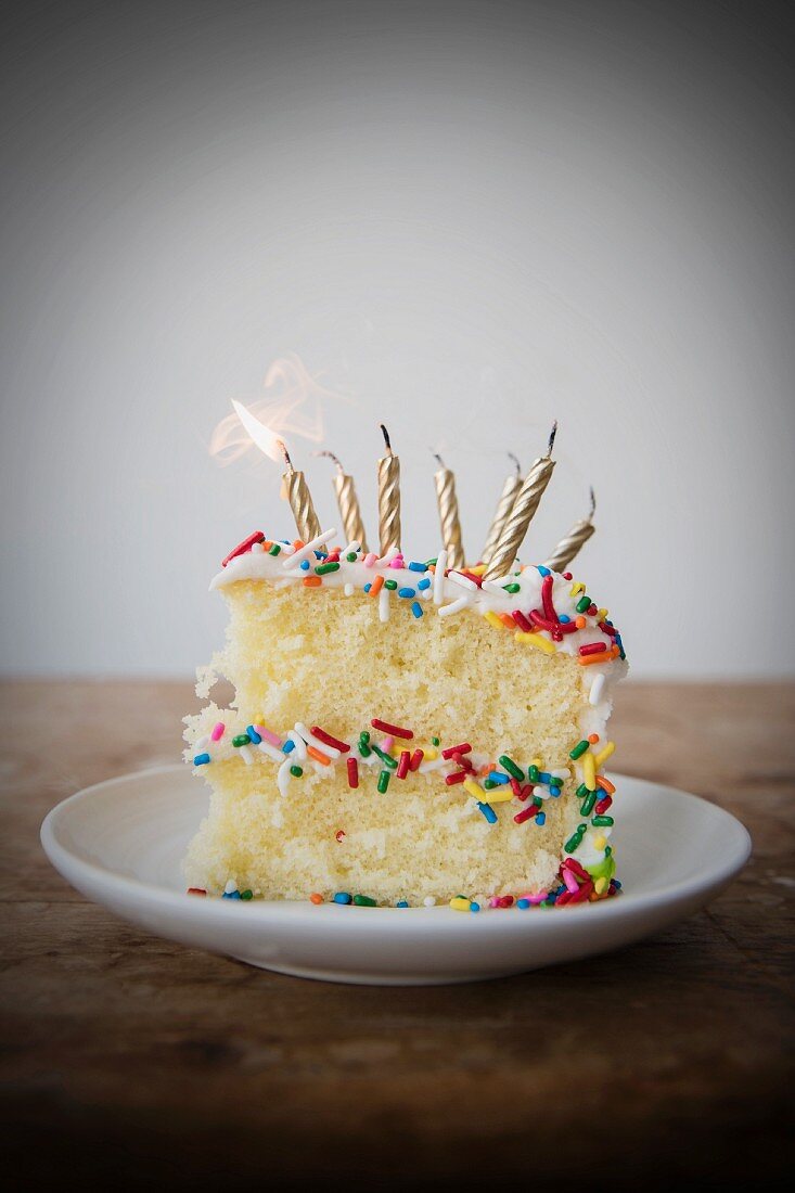 Flickering candle burning cake with sprinkles on plate