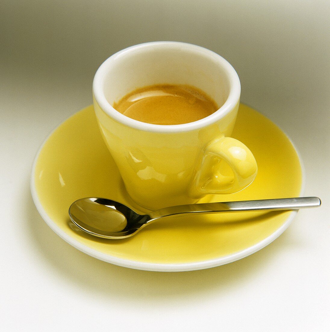 Eine gelbe Tasse Espresso mit Kaffeelöffel