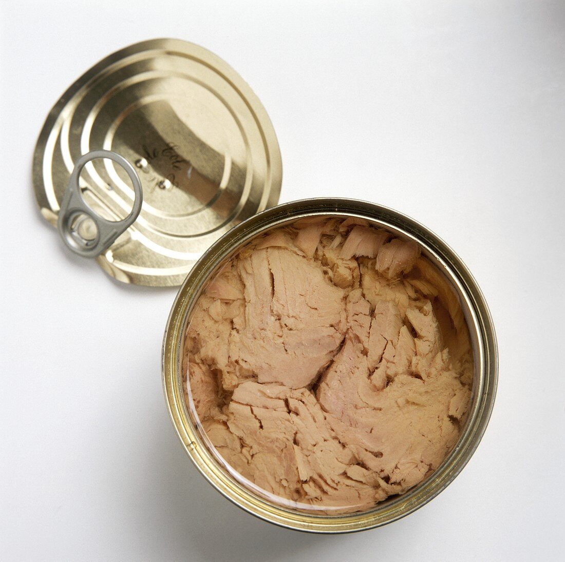 Tuna in an opened can, lid lying beside it