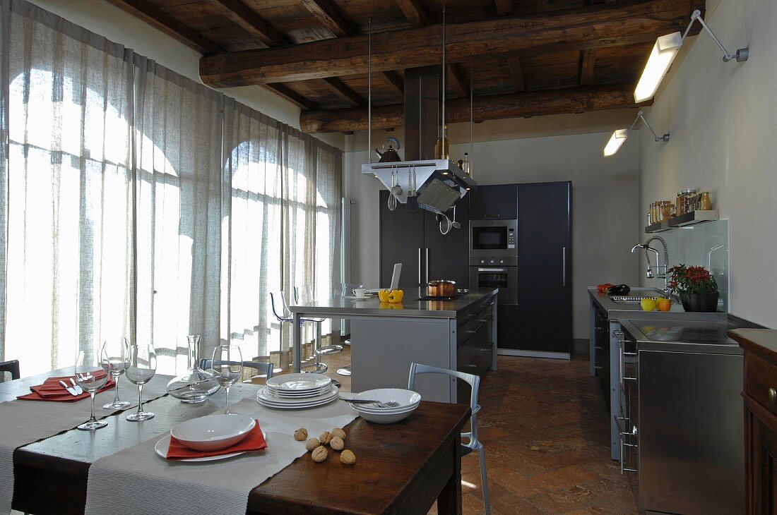 Modern, open-plan kitchen below rustic wood-beamed ceiling in renovated country house