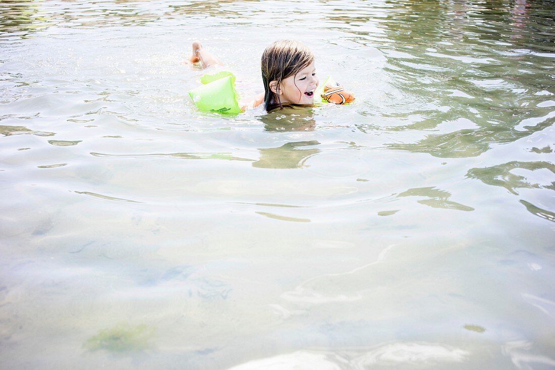 A little girl with armbands swimming in a lake