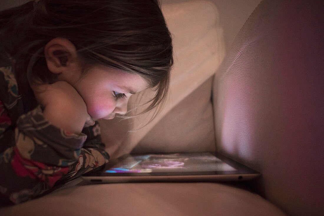 A little girl watching a film on a tablet in the dark