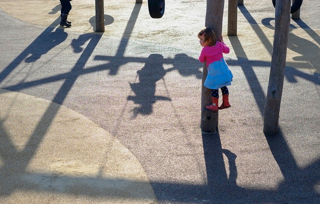 Kleines Mädchen auf Spielplatz klettert an Stamm hoch