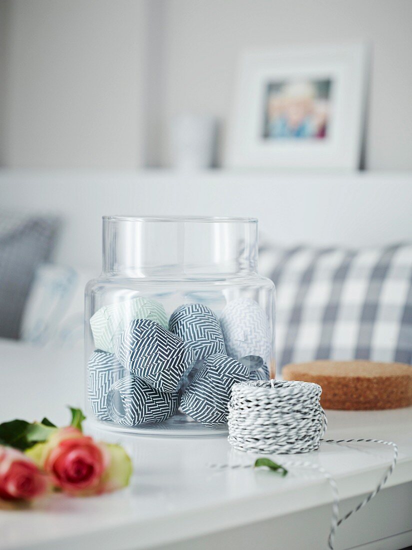 Various rolls of ribbons in a glass container on a table with a roll of black-and-white twine in the foreground