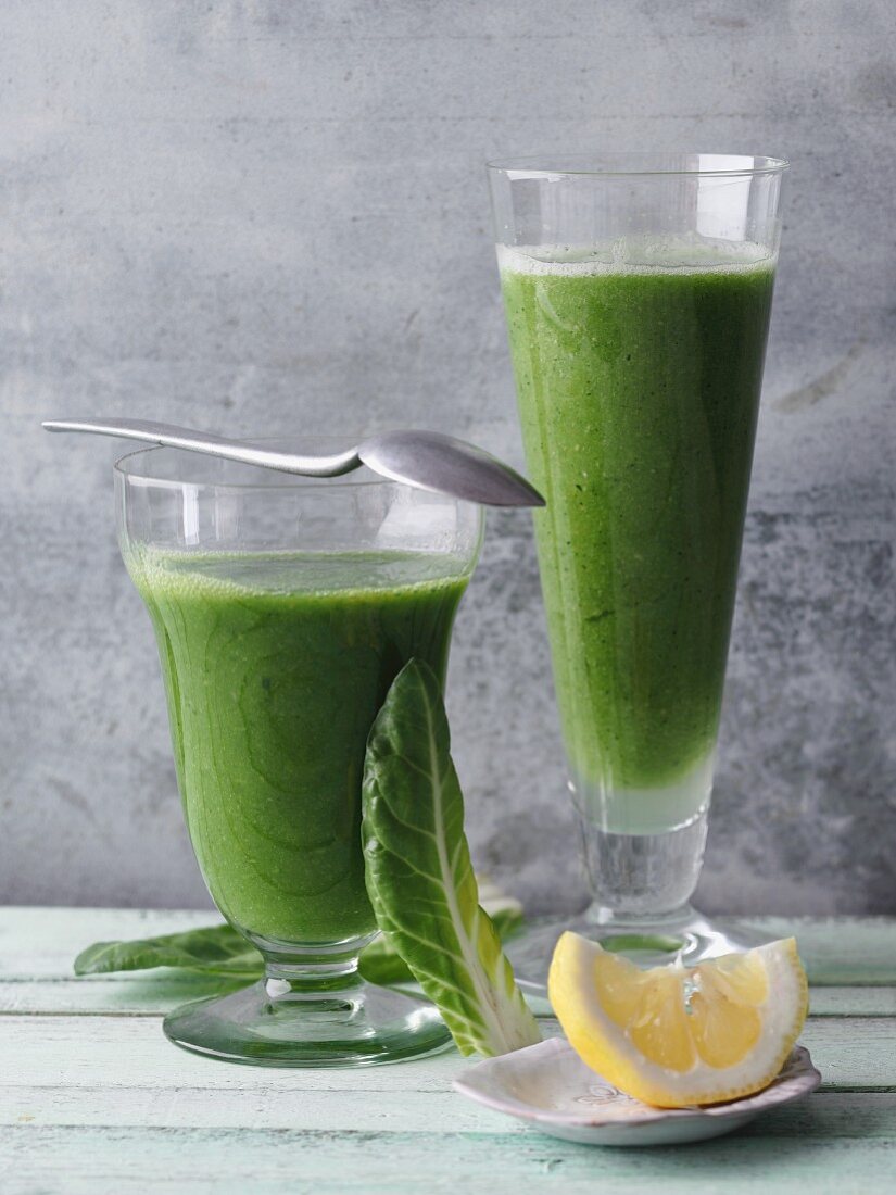 Two green smoothies garnished with chard and lemon