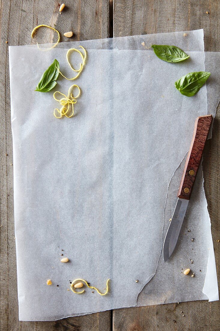 Baking paper, lemon zest, pine nuts and basil leaves on a rustic wooden table