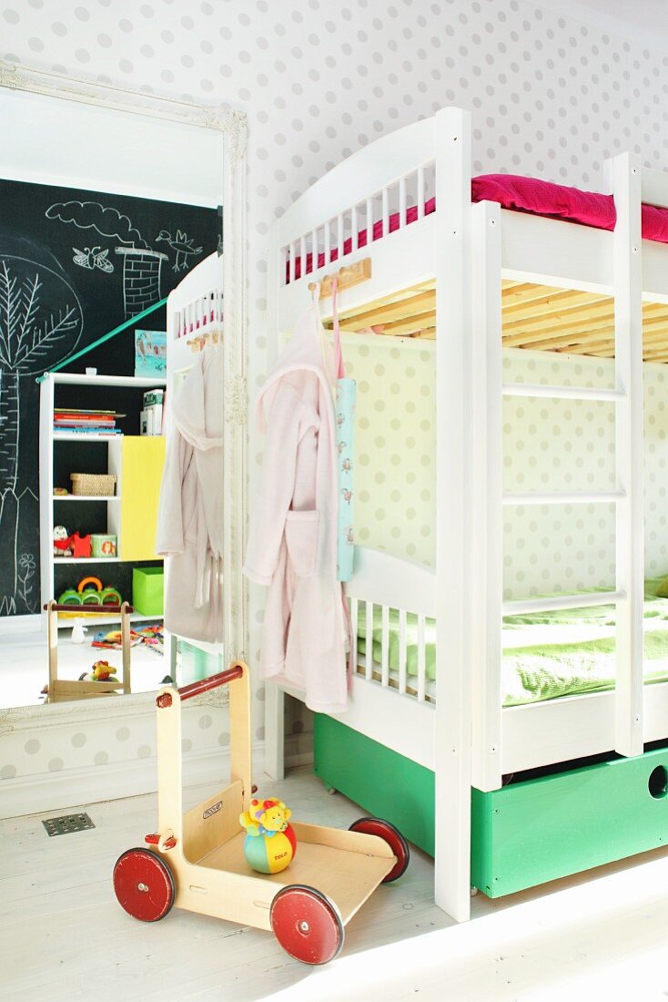 Kinderzimmer mit weißem Etagenbett und Lauflernwagen vor Wandspiegel