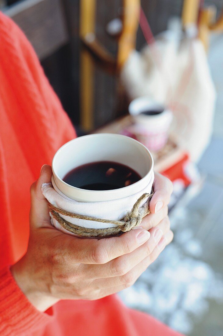 Hände halten umwickelten porzellanbecher mit Glühwein