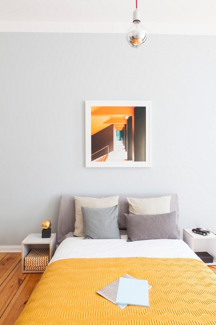 Bed against pale grey wall in bedroom in shades of yellow and grey