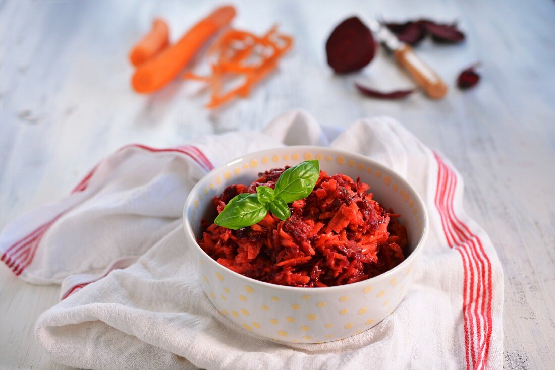 A bowl of beetroot salad with carrots and basil leaves
