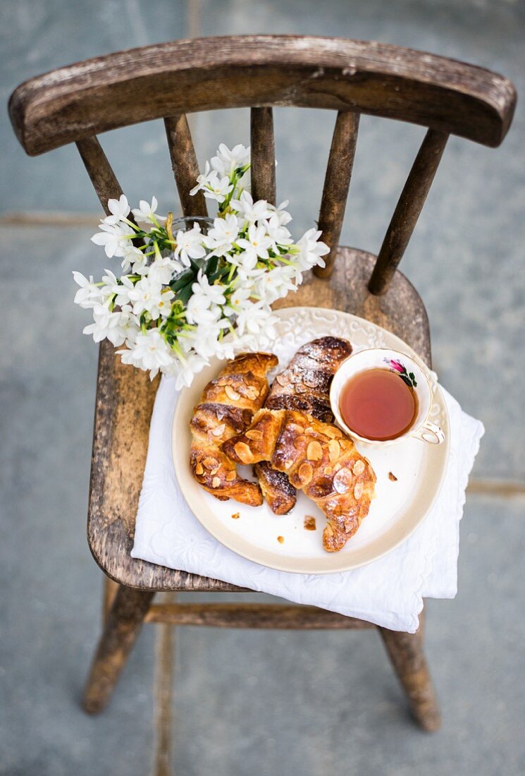 Homemade almond croissants with a cup of tea on rustic chair