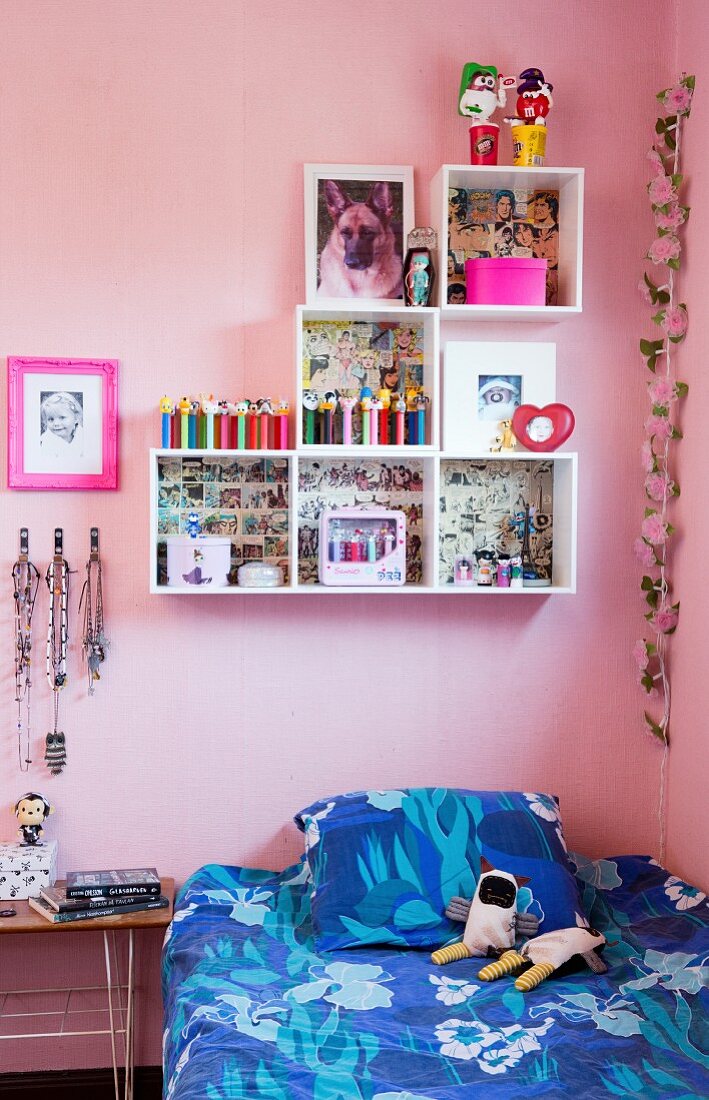 Bett mit blau gemusterter Bettwäsche und weiße Regalmodulen im Kinderzimmer mit rosa Wand