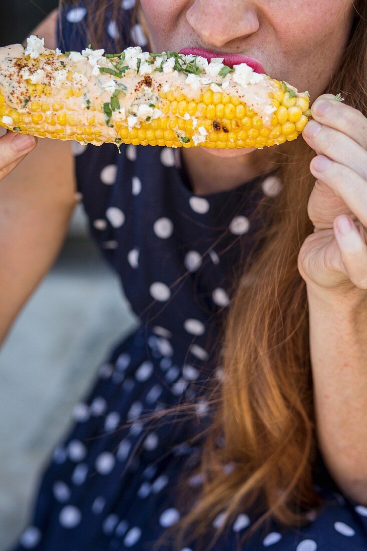 A woman eating elotes (grilled corn cobs, street food from Mexico)