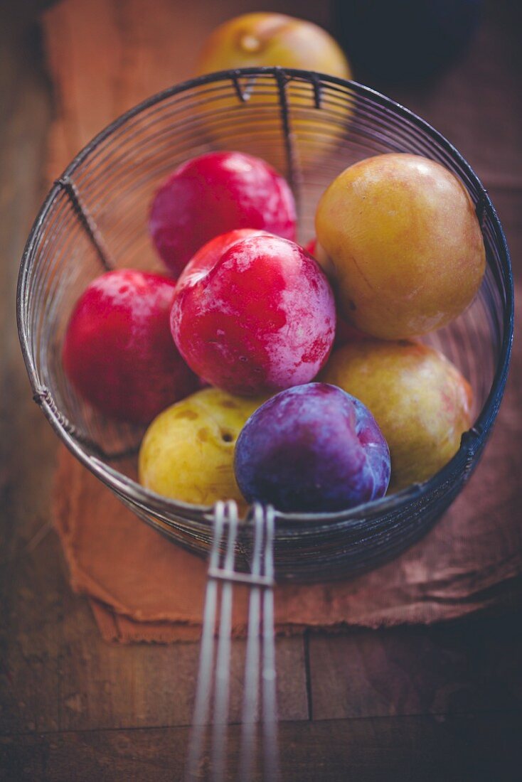 Various plums in a wire basket