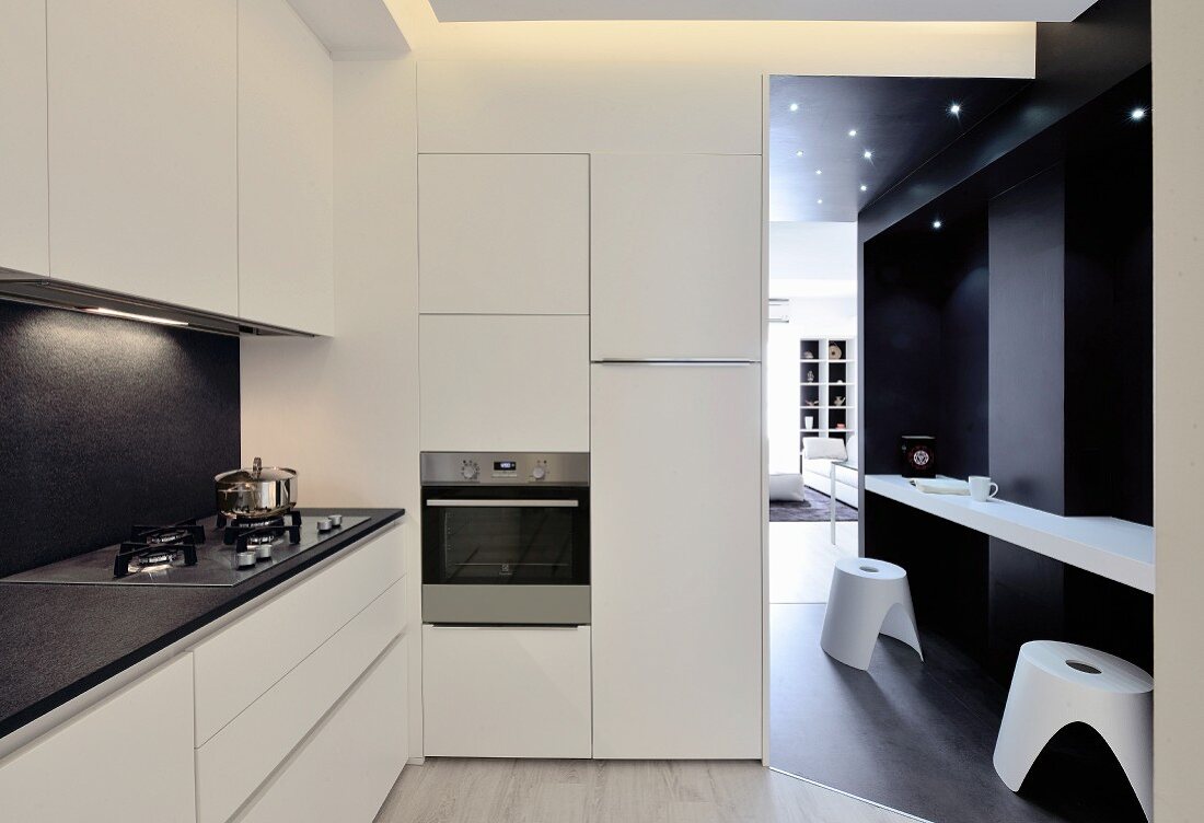 Breakfast bar and stools against dark wall in doorway leading from white minimalist designer kitchen