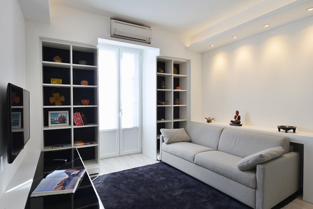 Pale couch, black rug and balcony door between white fitted shelves in modern living room