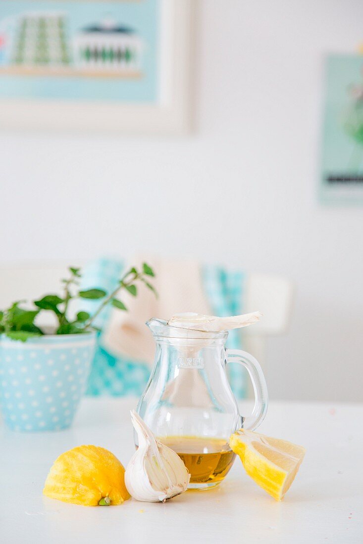 An arrangement of lemons, garlic, a carafe of olive oil and a pot of mint