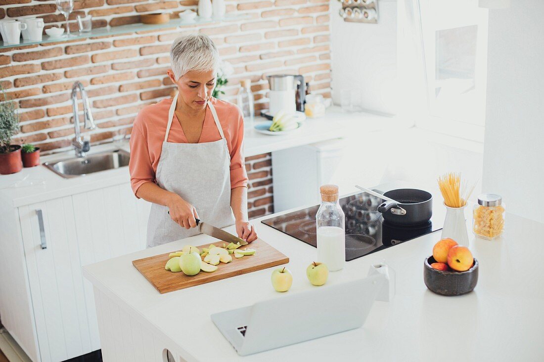 An older woman cutting apples in a modern kitchen