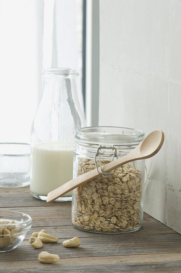 Müslizutaten: Haferflocken in Vorratsglas, Milchflasche und Cashewnüsse