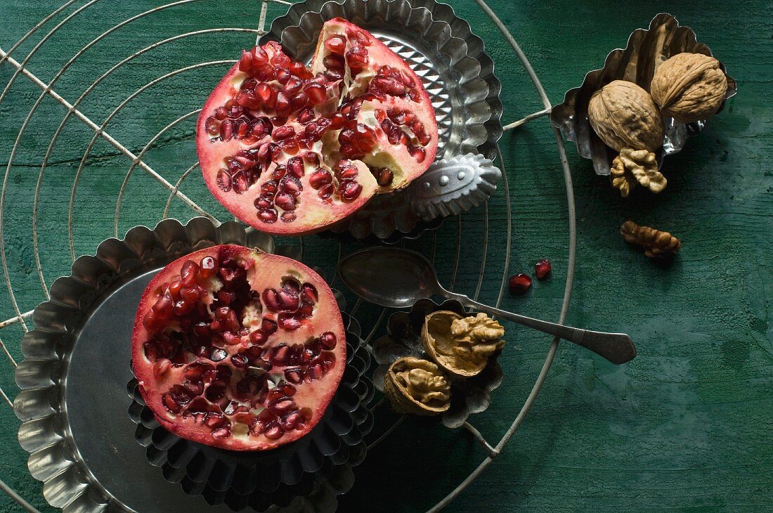 A halved pomegranate with a baking tin and walnuts on a wire rack