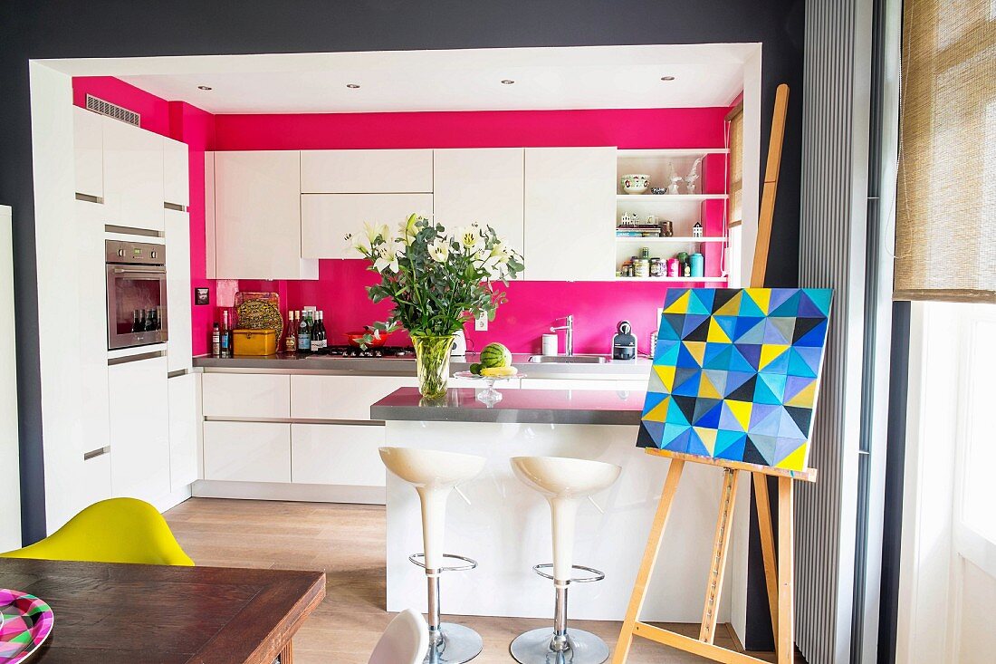 Open-plan kitchen with white, modern furnishings and hot pink walls