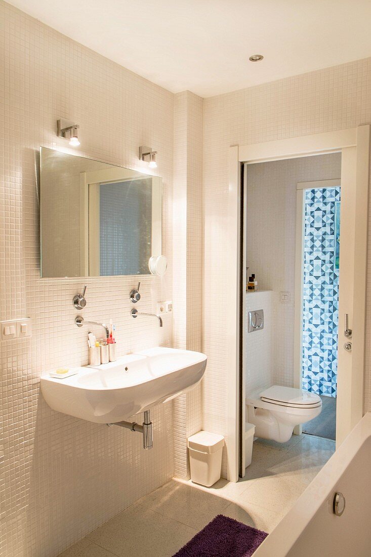 Badezimmer mit weißen Mosaikfliesen und Schiebetür zum WC