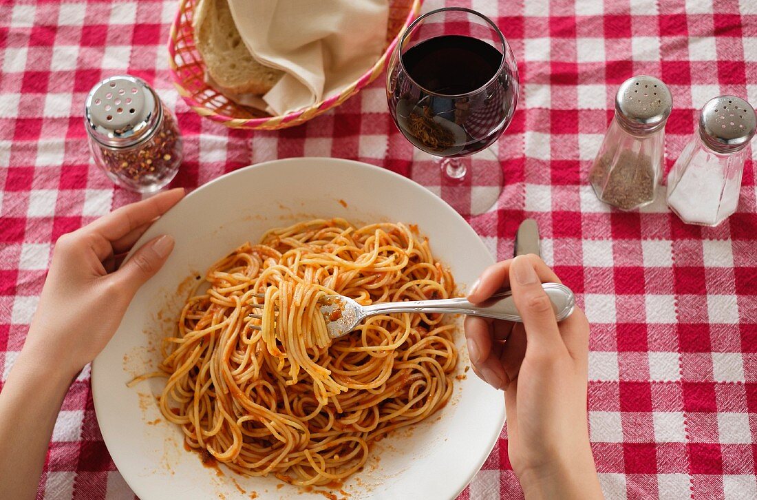 A person eating spaghetti with tomato sauce