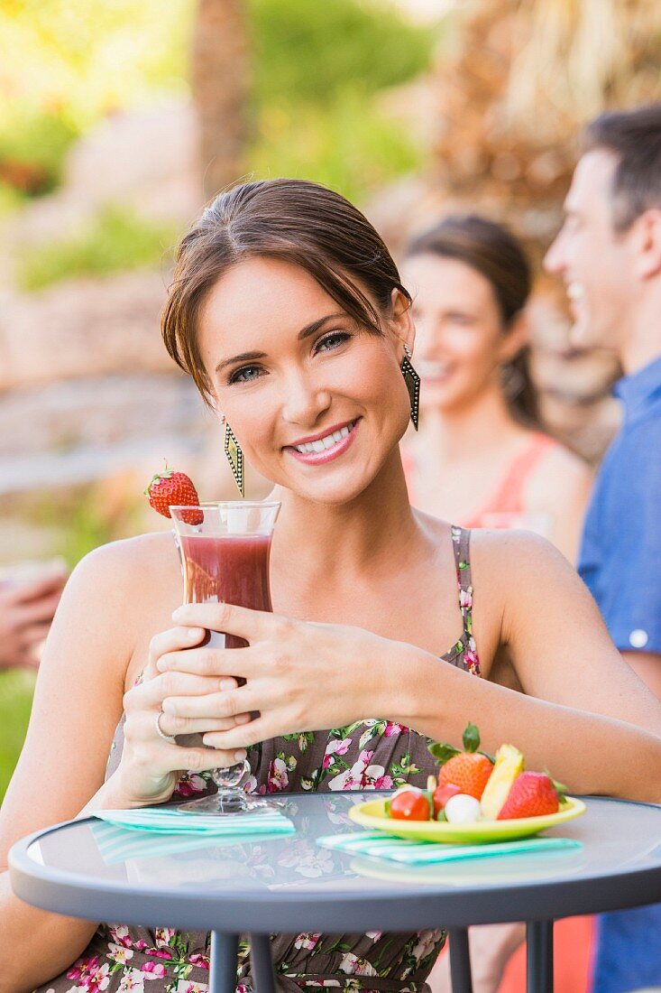 Frau mit Cocktail an Tisch im Freien