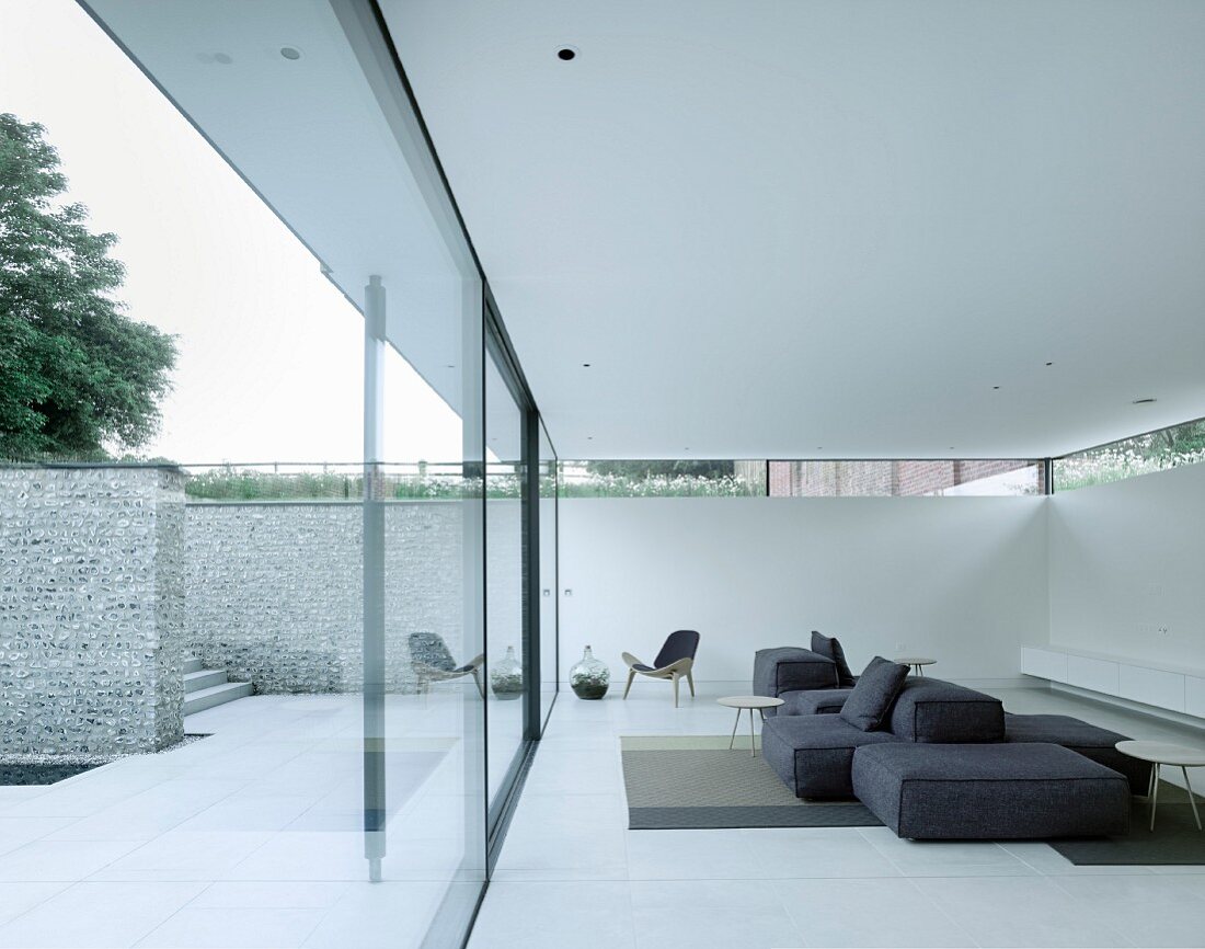 Minimalist designer furnishings in lounge area of white luxury apartment with glass wall, terrace and stone wall