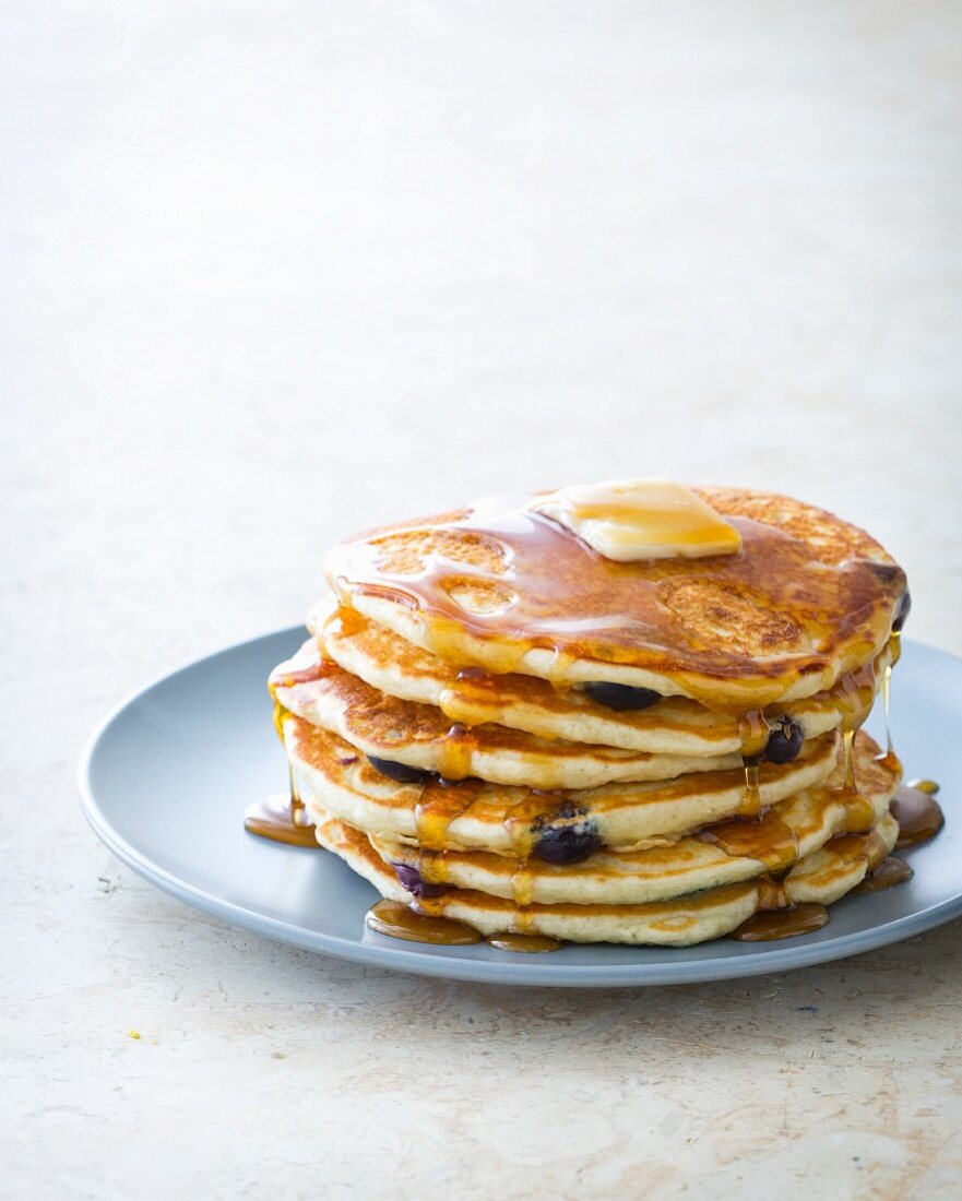 A stack of blueberry pancakes on a plate with maple syrup and butter