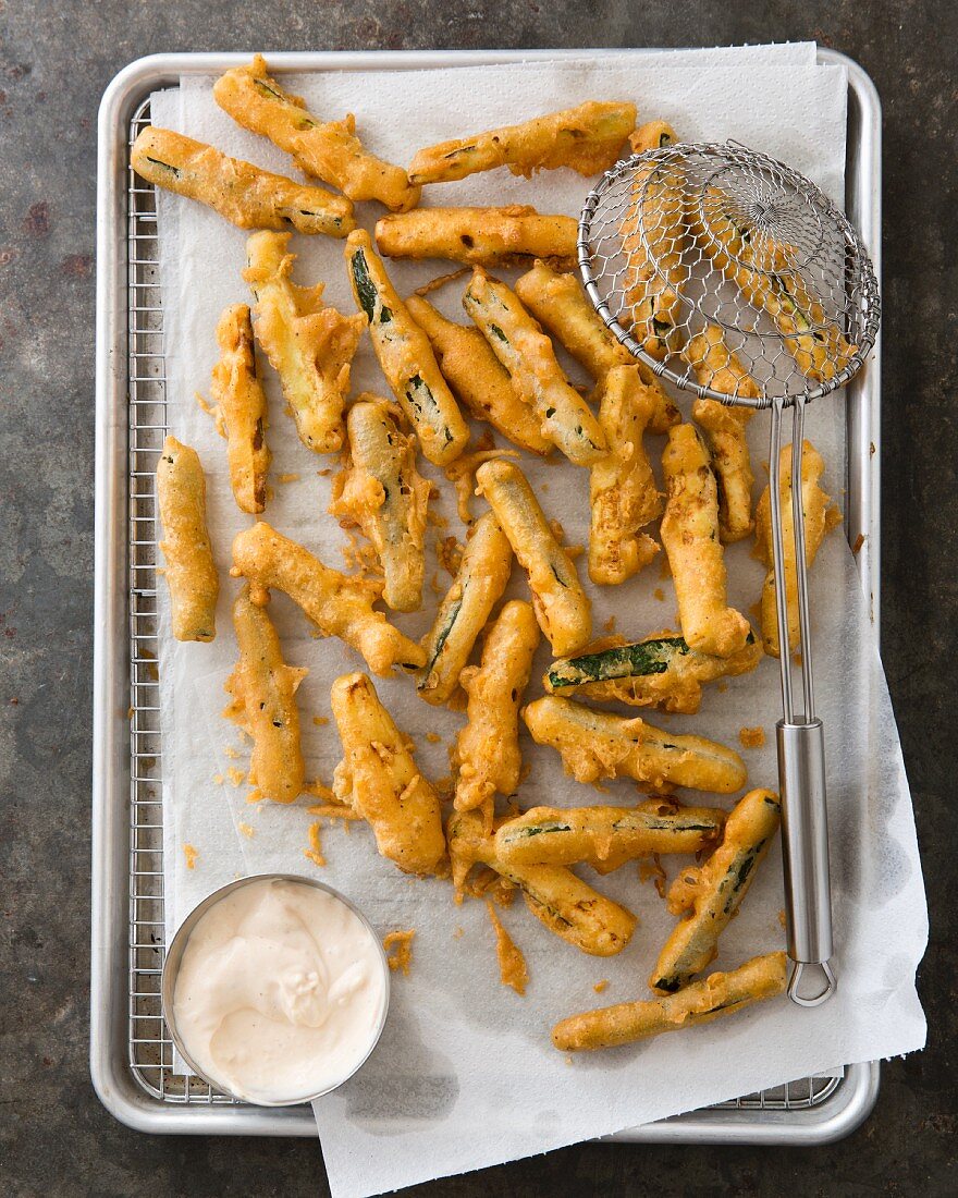 Deep-fried courgette sticks on kitchen paper with a dip