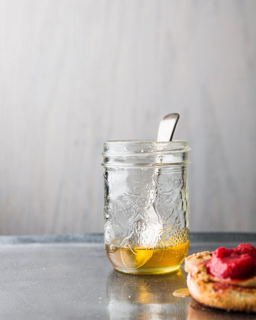 Honey in a jar with a spoon and an English muffin with raspberry jam