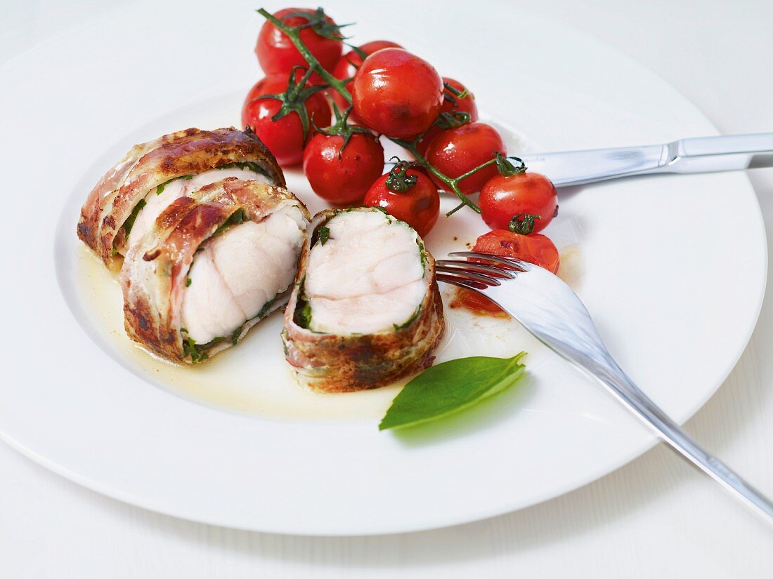 Fish wrapped in bacon served with vine tomatoes