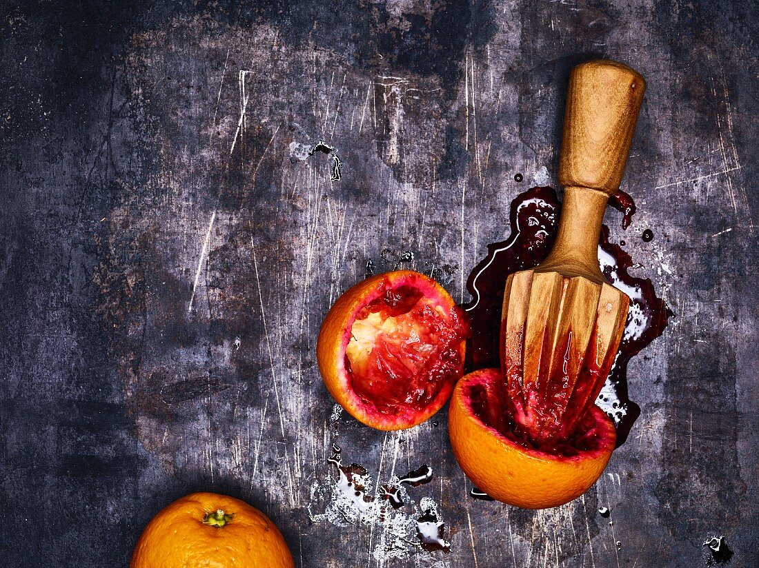 Juiced blood oranges with a wooden citrus juicer on a metal surface