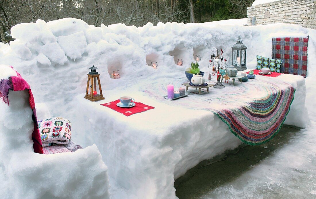 Candles and lanterns arranged on table sculpted from snow on snow-covered terrace
