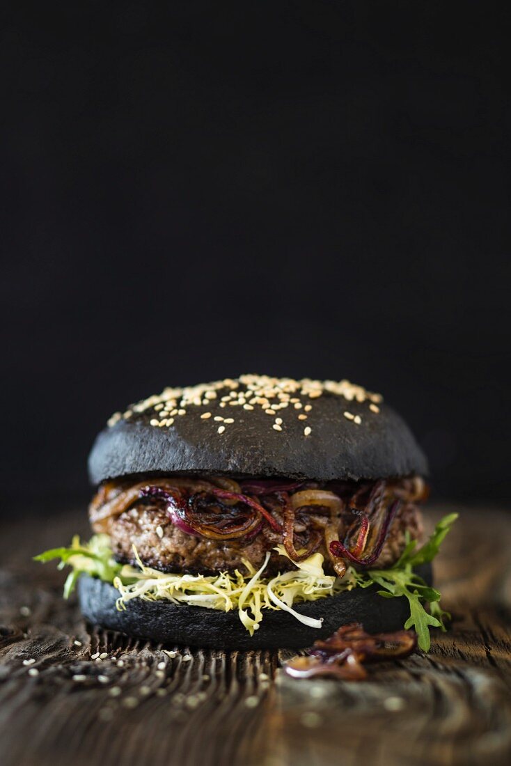 A dry aged hamburger with fried red onions and a black bun