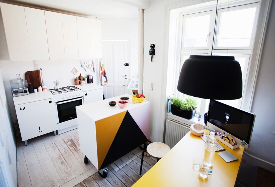 Küche mit halbhohem Schrank auf Rollen und gelber Tischplatte mit Computerbildschirm in Altbauwohnung