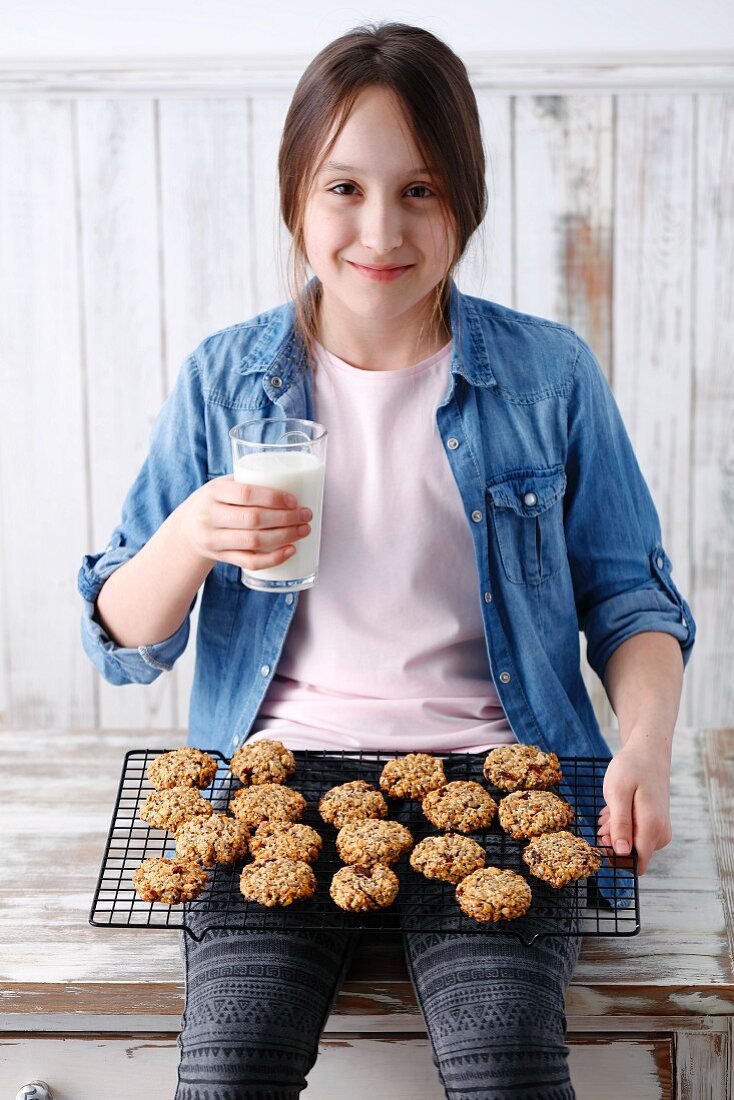 A girl sitting with freshly baked muesli biscuits and a glass of milk