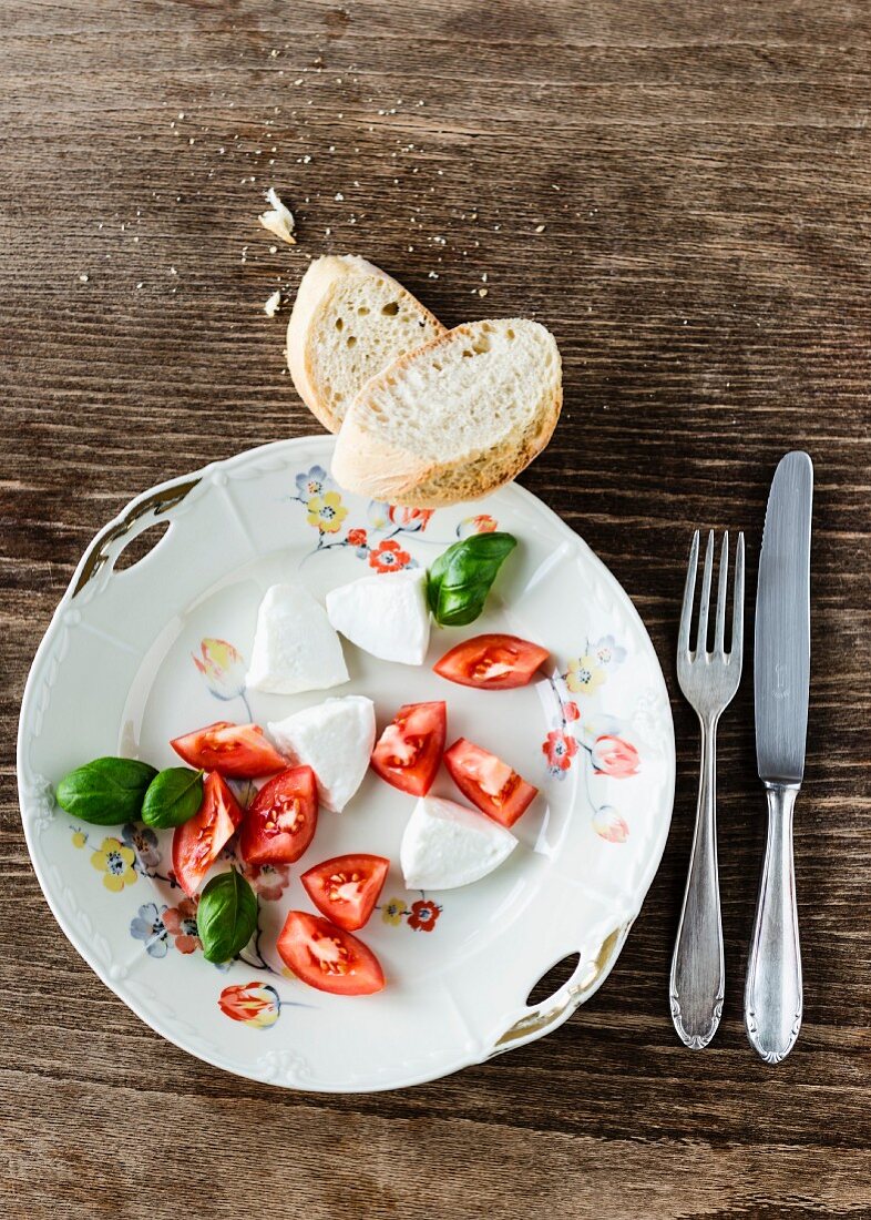 Mozzarella, Tomatenstücke, Basilikum und Baguette auf altem Porzellanteller mit Blumendekor