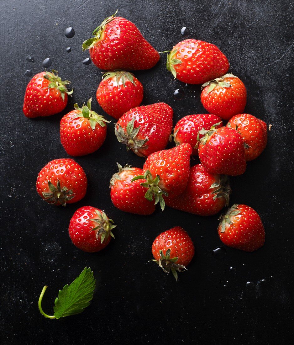 Fresh strawberries with a leaf on a black baking tray