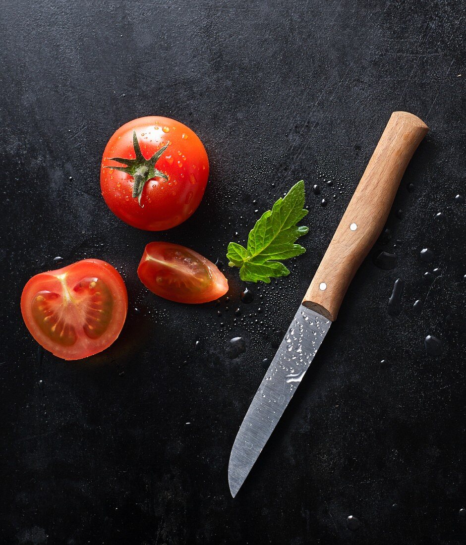 Zwei frische Tomaten mit Messer auf schwarzem Blech