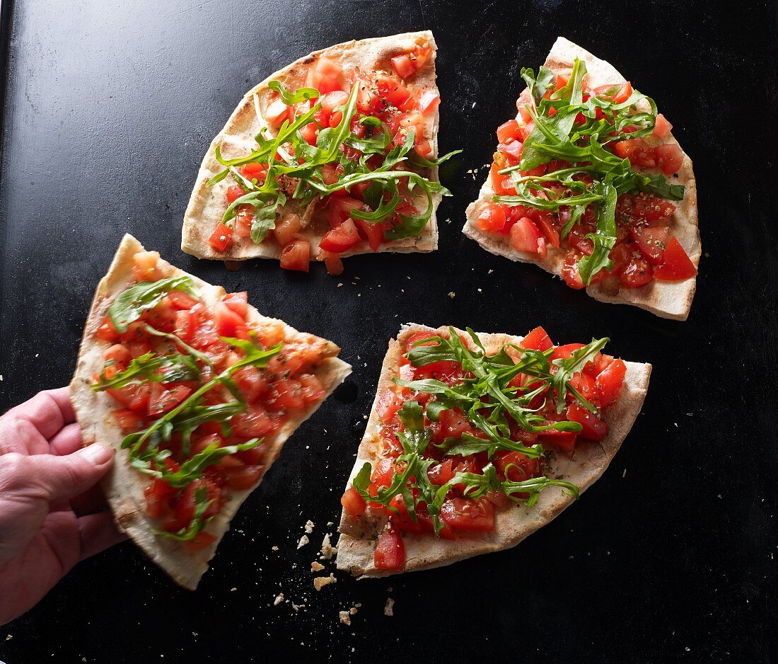 Hand greift Pizzastück von geschnittener Pizza-Bruschetta