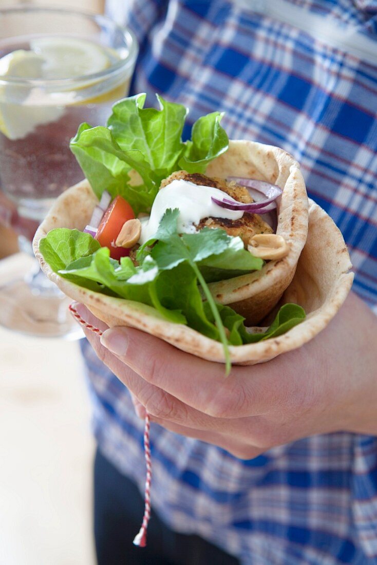 A hand holding a falafel, peanut and red onion wrap