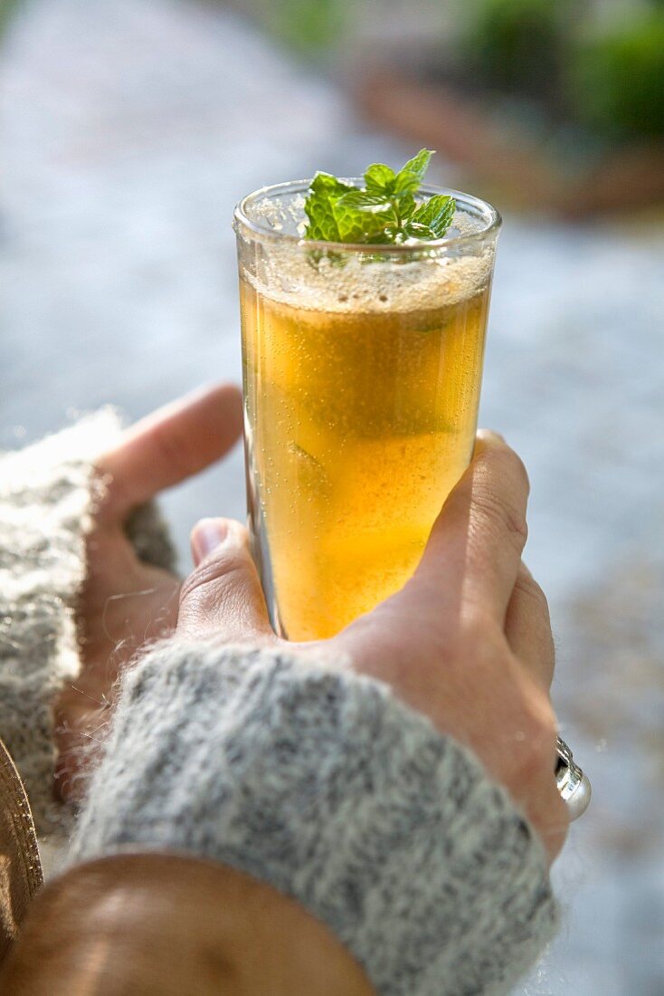 Hands holding a glass of apple juice with mint